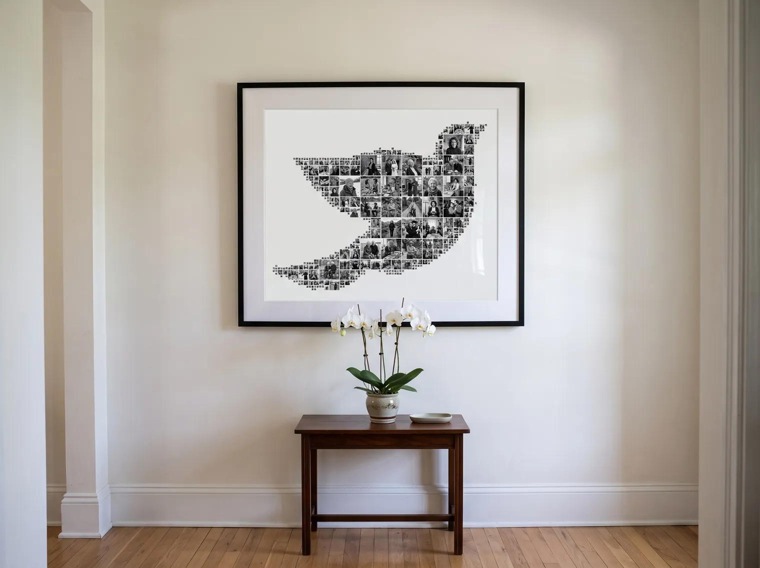 The black-and-white dove collage in a slim black frame with a wide white mat on a pale hallway wall above a small table with white orchids