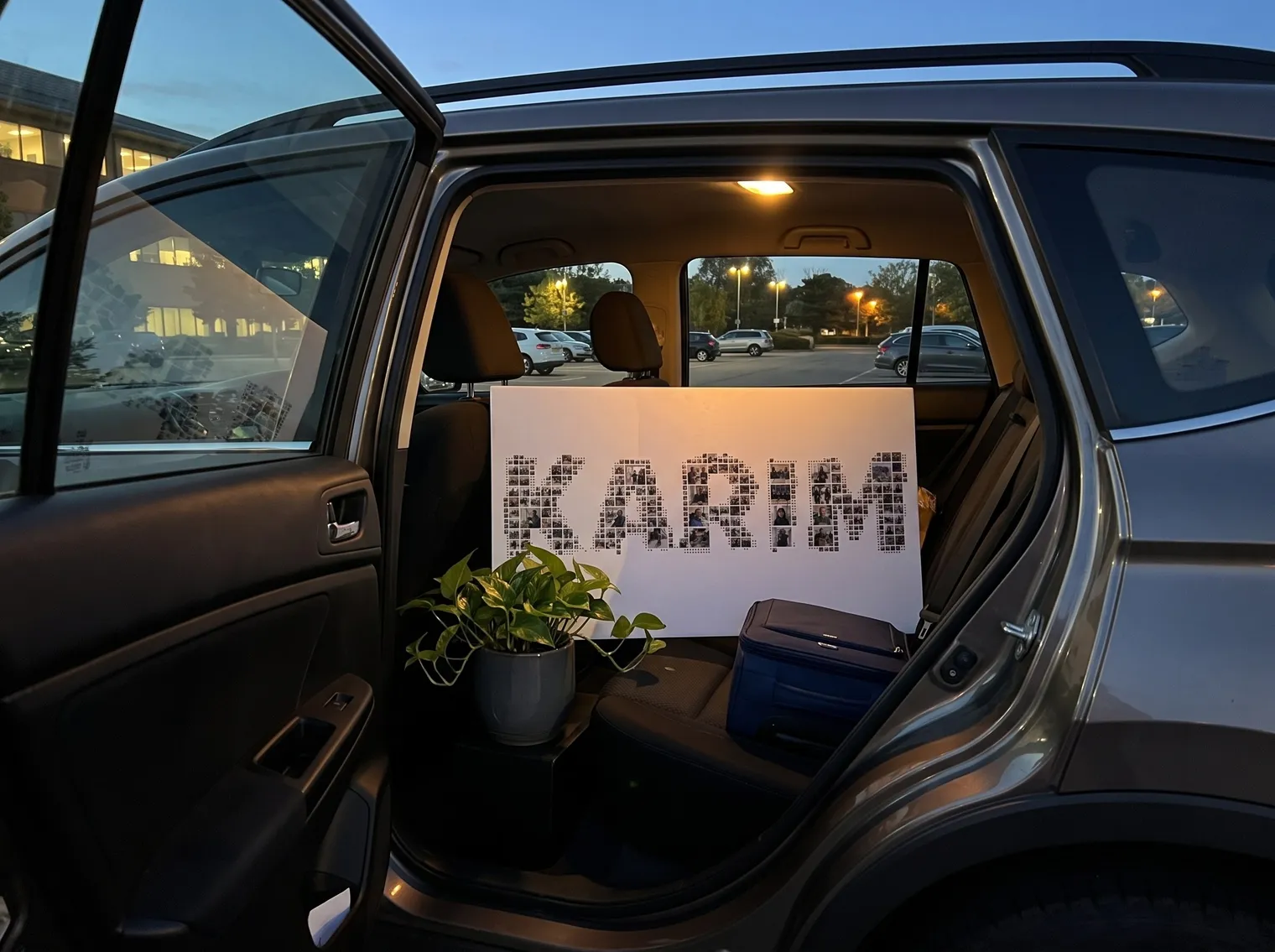 KARIM name photo collage on foam board on the back seat of a car with a suitcase and a potted plant, a farewell send-off