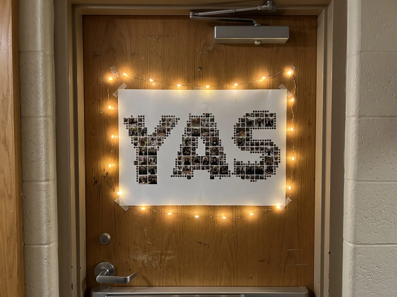 The YAS name photo collage as a poster on a dorm room door framed by fairy lights