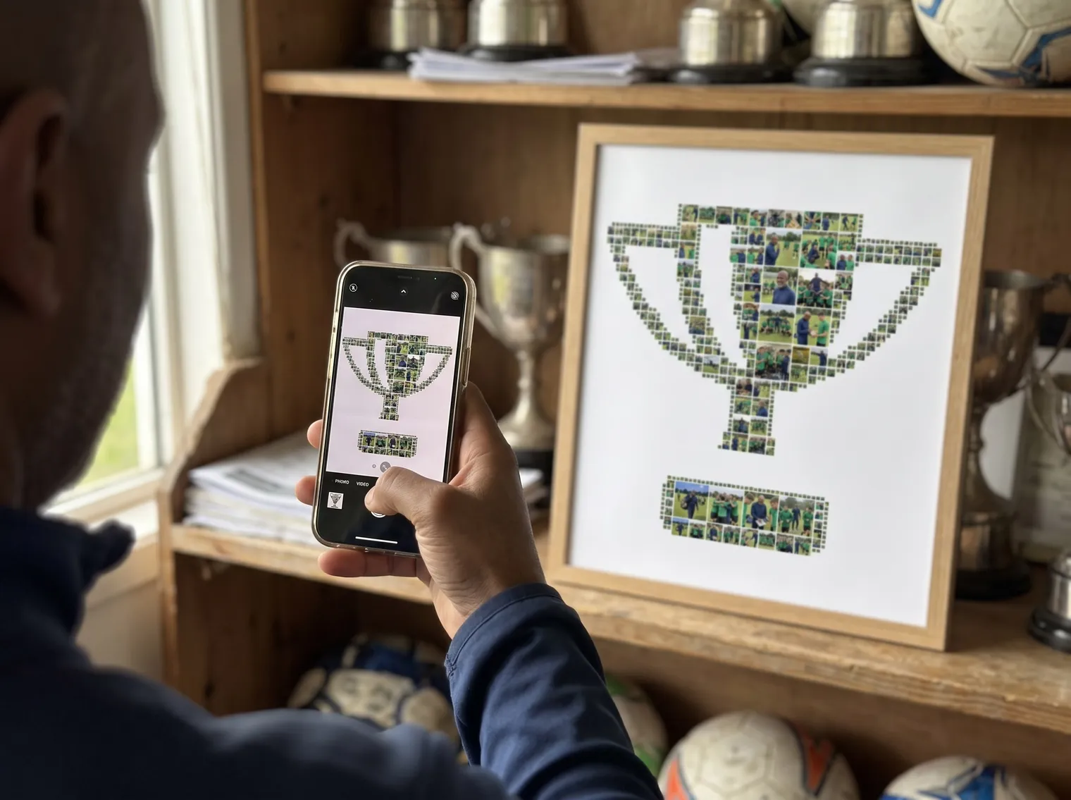 Person photographing the framed trophy photo collage on a clubhouse shelf with a phone